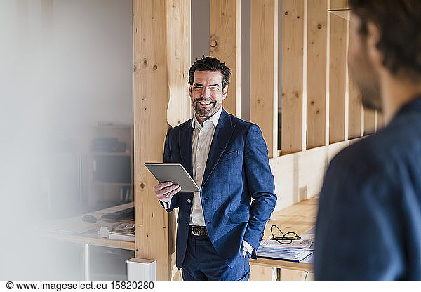 Smiling businessman holding tablet in wooden open-plan office