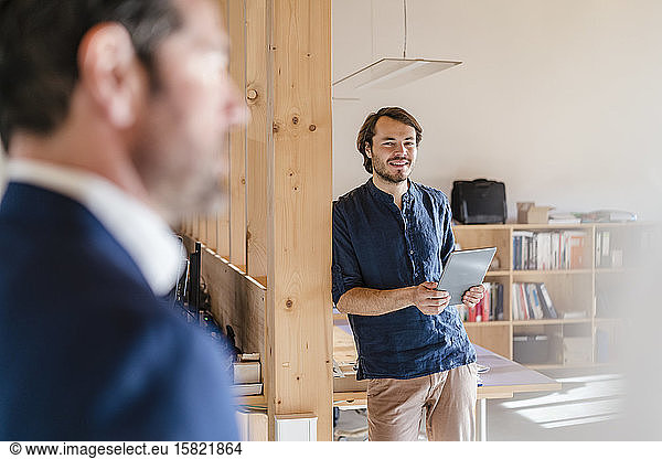 Smiling businessman holding tablet in wooden open-plan office