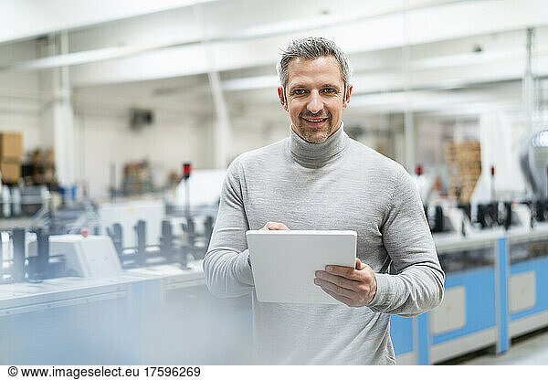 Smiling businessman holding tablet PC in factory