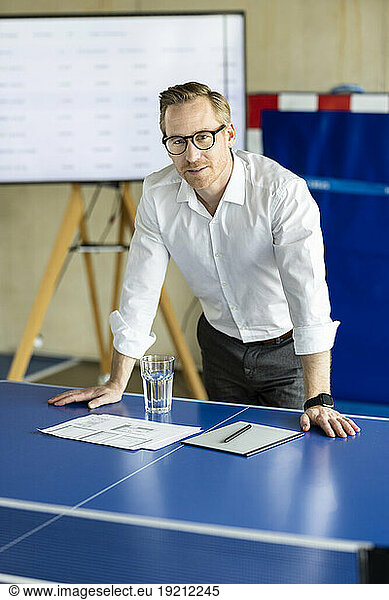 Smiling businessman leaning on tennis table in office