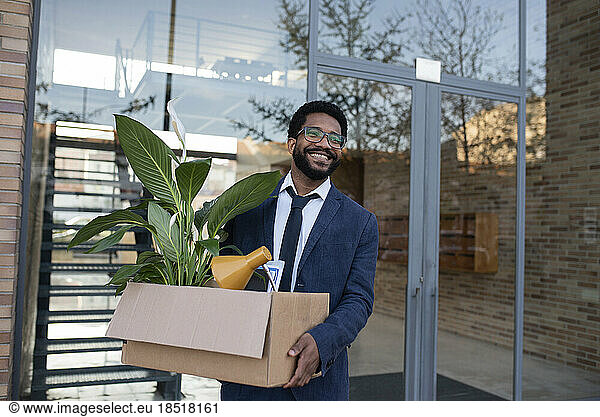 Smiling businessman leaving office building carrying cardboard box