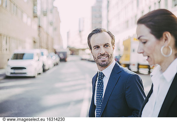 Smiling businessman looking at coworker while walking in city
