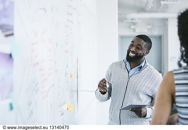 Smiling businessman looking at whiteboard while holding tablet computer in office