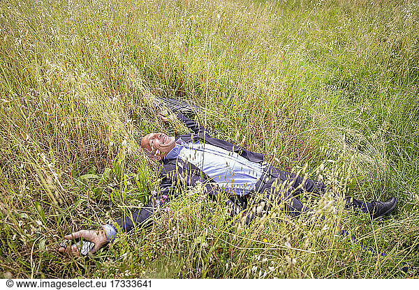 Smiling businessman lying down while relaxing on grassy field
