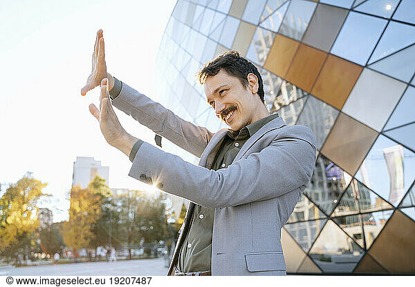 Smiling businessman making finger frame in front of office building