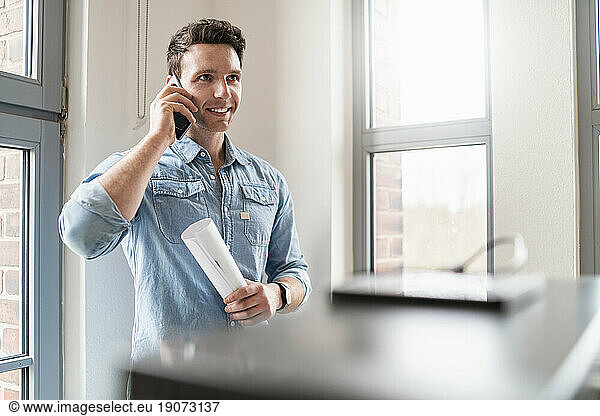 Smiling businessman on cell phone at the window in office