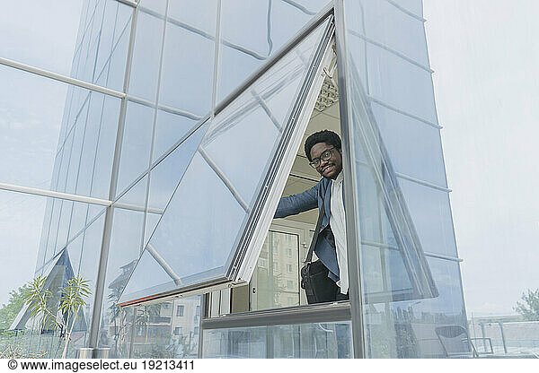 Smiling businessman opening window of office building