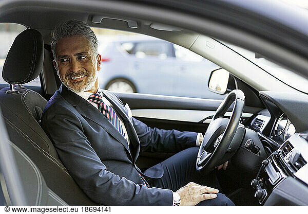 Smiling businessman sitting on driver's seat in car