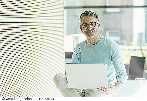 Smiling businessman sitting with laptop in office