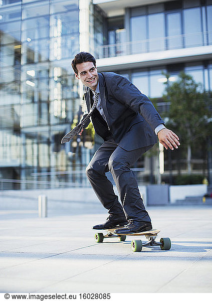 Smiling businessman skateboarding outside urban building