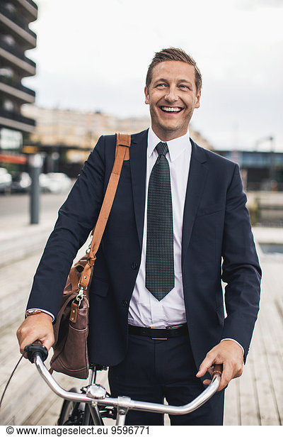 Smiling businessman standing with bicycle in city