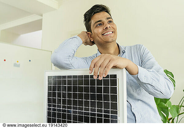Smiling businessman standing with solar panel model at office