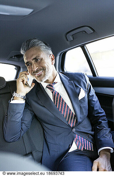 Smiling businessman talking on smart phone sitting in car