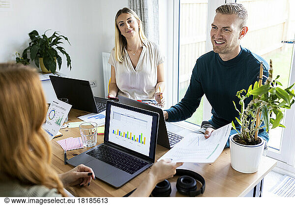 Smiling businessman talking to businesswoman and giving document in office