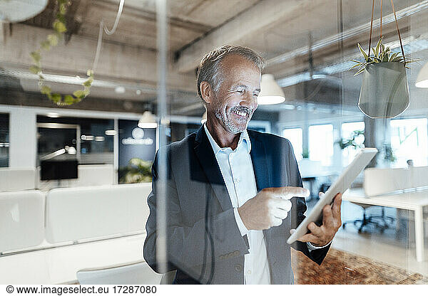 Smiling businessman using digital tablet behind glass wall