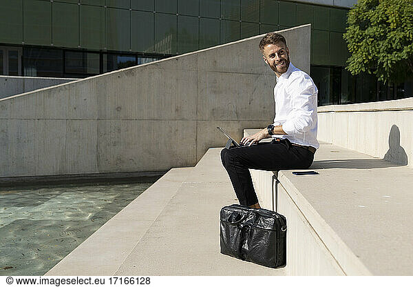 Smiling businessman using digital tablet while sitting on promenade
