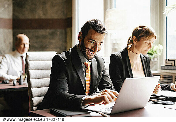 Smiling businessman using laptop working by businesswoman at desk in law office