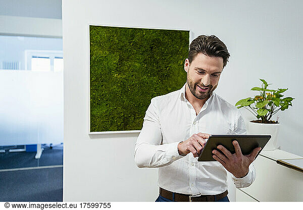 Smiling businessman using tablet PC in office