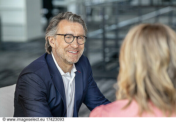 Smiling businessman wearing eyeglasses discussing with female colleague in office