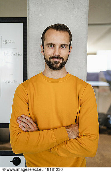 Smiling businessman with arms crossed leaning on column at workplace