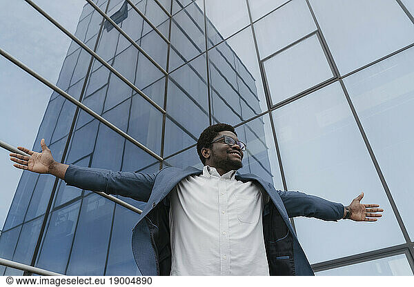 Smiling businessman with arms outstretched in front of glass building