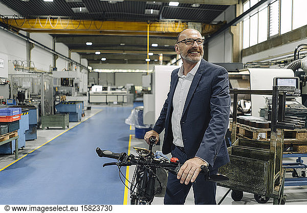 Smiling businessman with bicycle in a factory