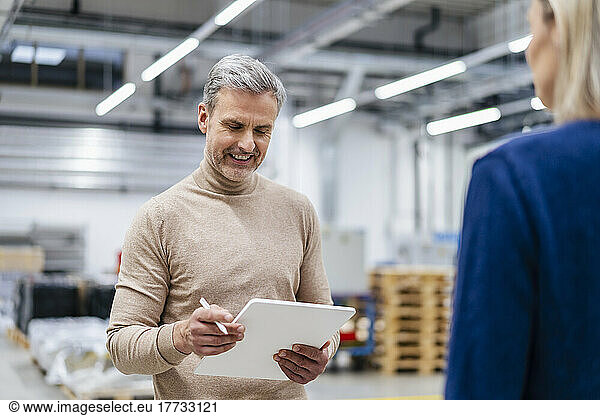 Smiling businessman with digital tablet and businesswoman in factory