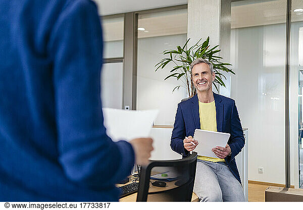 Smiling businessman with digital tablet looking at businesswoman in office