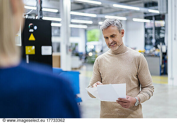 Smiling businessman with documents and businesswoman in factory