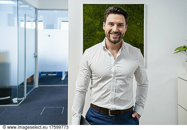 Smiling businessman with hand in pocket at office