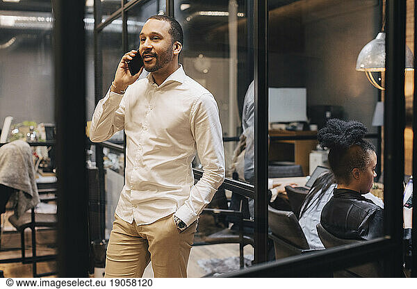 Smiling businessman with hand in pocket talking on mobile phone at office