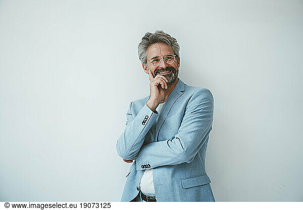 Smiling businessman with hand on hip standing in front of wall