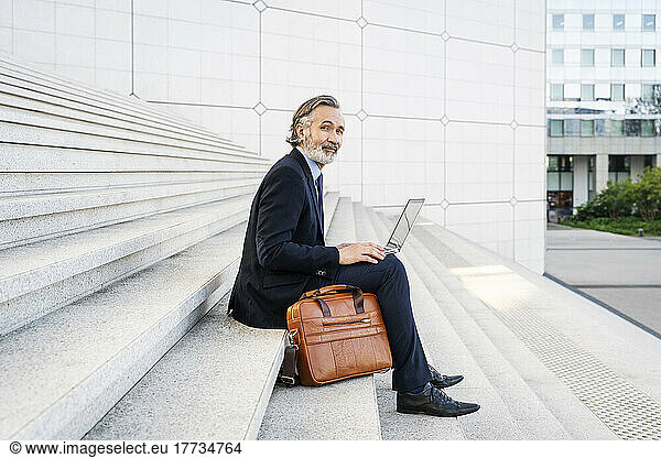 Smiling businessman with laptop sitting on steps