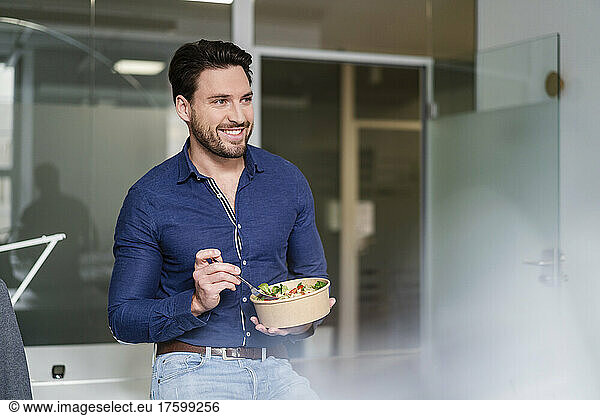 Smiling businessman with salad bowl taking break in office