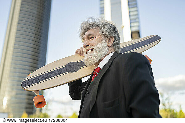 Smiling businessman with skateboard in city