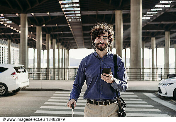 Smiling businessman with smart phone crossing road