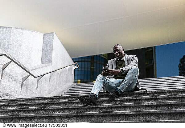 Smiling businessman with smart phone sitting on steps in subway