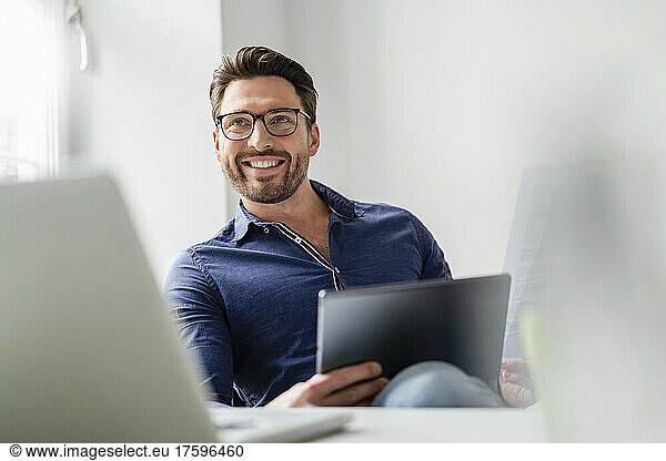 Smiling businessman with tablet PC wearing eyeglasses in office
