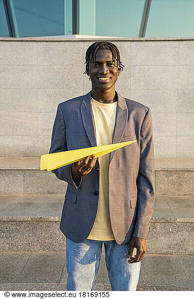 Smiling businessman with yellow paper airplane in front of steps