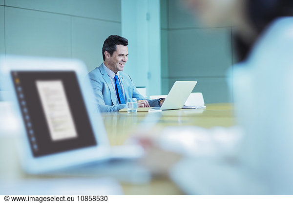 Smiling businessman working at laptop in conference room