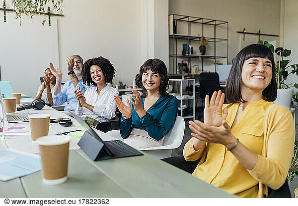 Smiling businessmen and businesswoman clapping hands at desk in office