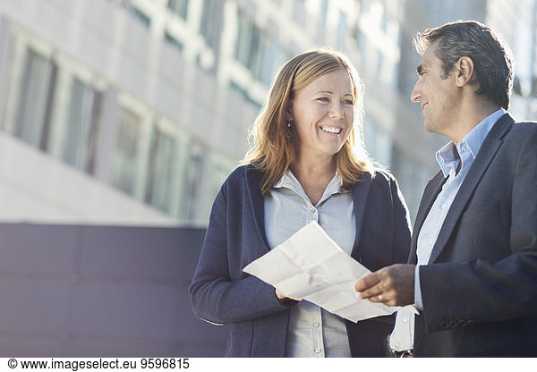 Smiling businesspeople discussing over document outside office building