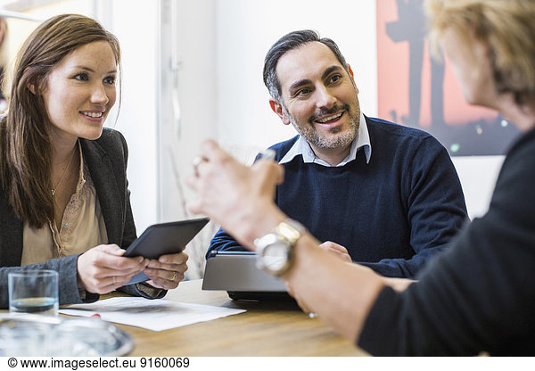 Smiling businesspeople with digital tablets discussing at desk in office