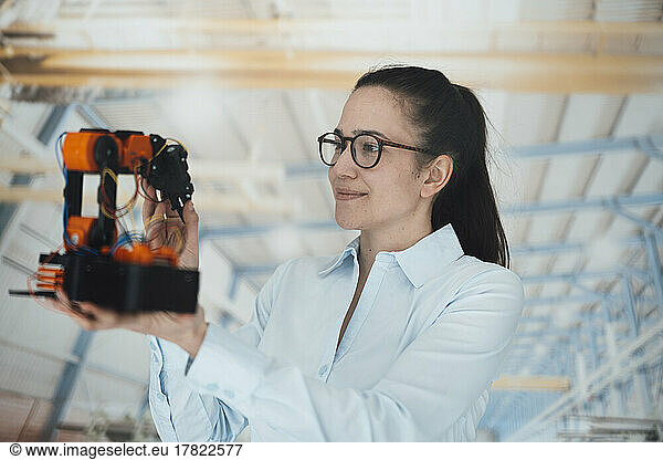 Smiling businesswoman analyzing robotic arm model in industry