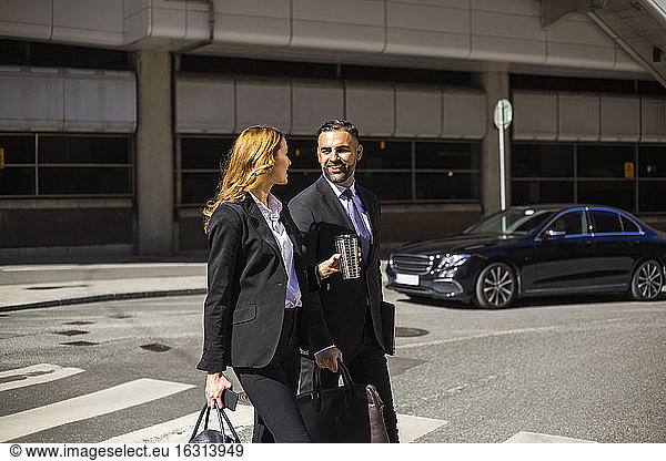 Smiling businesswoman and businessman crossing road in city
