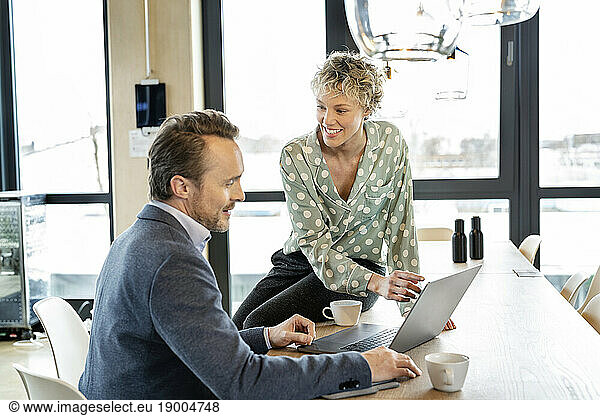 Smiling businesswoman and businessman discussing over laptop