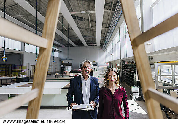 Smiling businesswoman and businessman looking at wooden structure in factory
