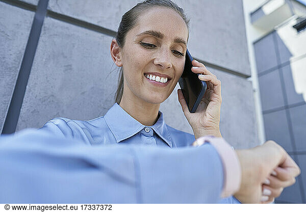 Smiling businesswoman checking smart watch while talking on mobile phone