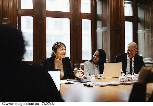 Smiling businesswoman discussing strategy with colleagues in board room at law office
