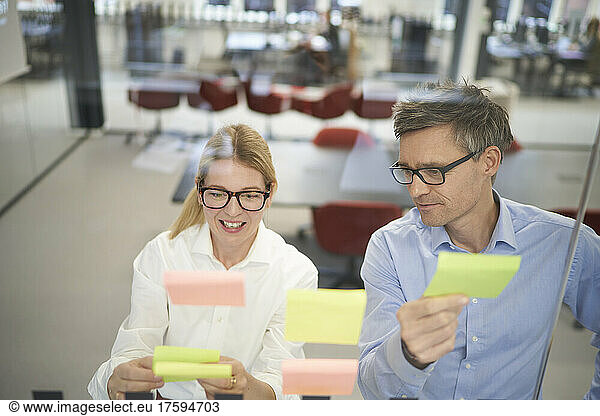 Smiling businesswoman discussing with colleague over adhesive note in meeting room
